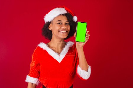 Téléchargez les photos : Belle femme brésilienne noire, habillée comme Santa Claus, maman Claus, montrant écran de smartphone - en image libre de droit