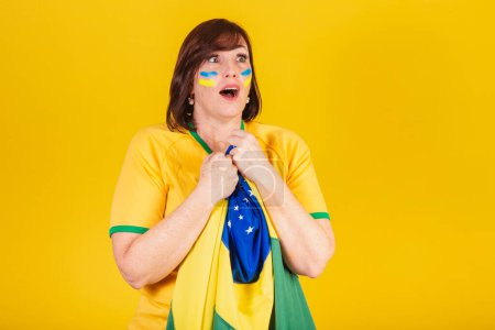 Téléchargez les photos : Femme rousse, fan de football brésilien. flottant avec le drapeau du Brésil, surpris. - en image libre de droit