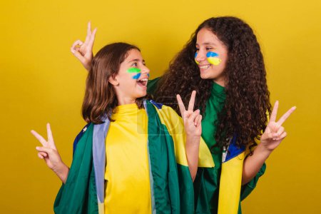Photo for Sisters and friends supporters of Brazil, football fans, posing for a photo, fingers of peace and love, fun photo, smiling. World Cup. Olympics. - Royalty Free Image