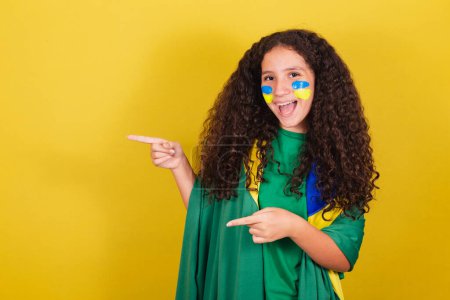 Photo for Brazilian, Caucasian, football fan girl pointing to the side, showing negative space for text, advertisement, advertisement, .World Cup. Olympics. - Royalty Free Image