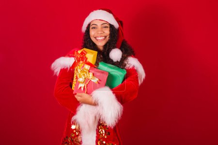 Téléchargez les photos : Belle femme noire brésilienne, habillée en Père Noël claus, vêtements de Noël. tenant trois cadeaux. - en image libre de droit