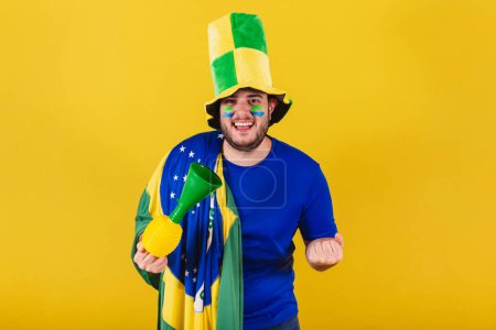 Photo for Brazilian caucasian man, soccer fan from Brazil, wearing hat and using horn, Celebrating victory of his team.Cheering in the championship. - Royalty Free Image