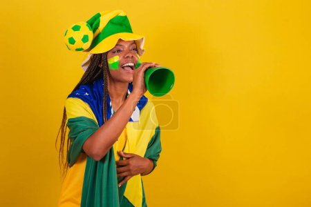 Téléchargez les photos : Femme noire jeune fan de football brésilien. en utilisant la prise de téléphone pour annoncer quelque chose. - en image libre de droit