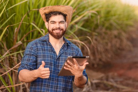 Foto de Hombre caucásico brasileño, agricultor, trabajador rural, ingeniero agrícola, sosteniendo la tableta y con el pulgar hacia arriba, positivo. Agricultura y tecnología. - Imagen libre de derechos