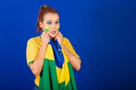 Photo for Caucasian woman, redhead, brazil soccer fan, brazilian, blue background, anxious and distressed with flag in hands - Royalty Free Image