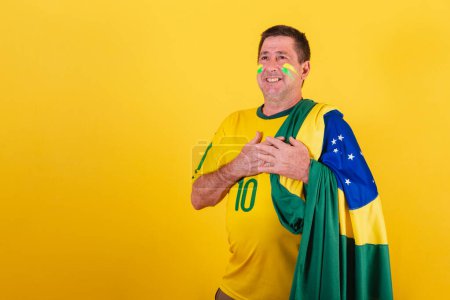 Téléchargez les photos : Homme adulte, fan de football brésilien, portant le drapeau, chantant l'hymne national - en image libre de droit