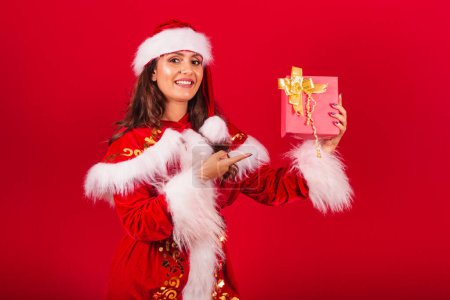 Photo for Brazilian woman dressed in Christmas clothes, Santa Claus. showing a red gift. - Royalty Free Image