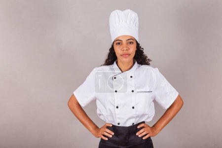 Téléchargez les photos : Jeune femme brésilienne noire, cuisinière, chef cuisinier. mains sur les hanches, optimiste et confiant. - en image libre de droit