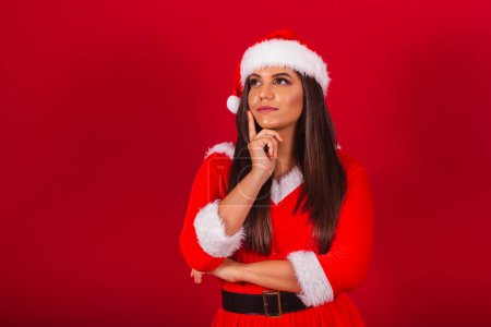 Photo for Beautiful Brazilian woman dressed in Christmas clothes, Santa Claus. doubt, questioning, thinking. - Royalty Free Image