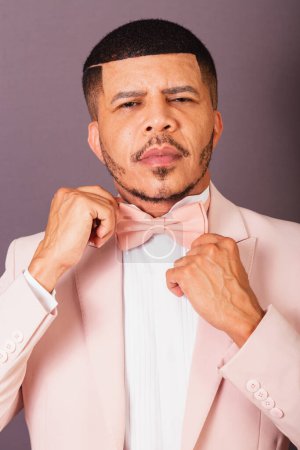 Photo for Brazilian black man, with pink suit and bow tie, gray background, holding his hands. - Royalty Free Image
