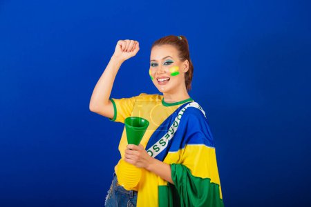 Téléchargez les photos : Femme caucasienne, rousse, fan de football brésilien, Brésilien, fond bleu, danse avec drapeau et corne - en image libre de droit