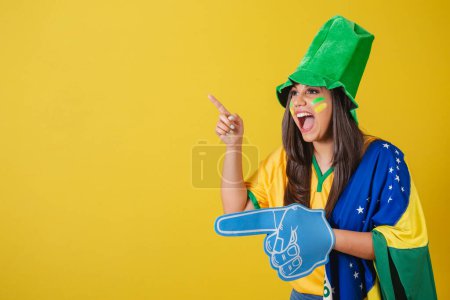 Photo for Woman supporter of Brazil, world cup 2022, pointing with foam finger to something in the distance. - Royalty Free Image