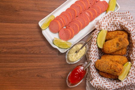 Photo for Chicken croquette and Cambu sausage, typical Brazilian snack,served with lemon slices, chili sauce and mayonnaise. on wooden table - Royalty Free Image
