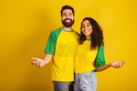 Foto de Pareja de aficionados al fútbol brasileño, vestidos con los colores de la nación, mujer negra, hombre caucásico. Bienvenida. Brazos abiertos - Imagen libre de derechos