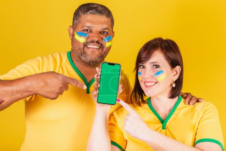 Photo for Couple, red-haired woman and black man, Brazilian soccer fans. Smartphone, online mobile. - Royalty Free Image