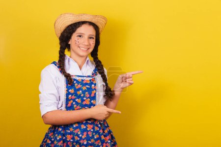 Photo for Girl wearing typical clothes for Festa Junina. pointing to the side with fingers, space for ad and text. For the Arraia party - Royalty Free Image