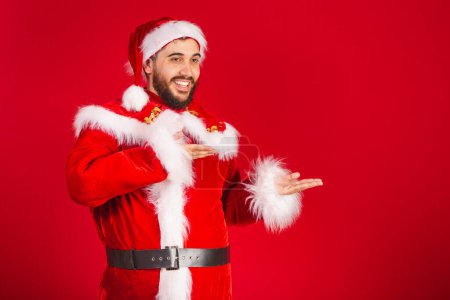 Foto de Hombre brasileño, vestido con ropa de Santa Claus, presentando producto o texto a la derecha - Imagen libre de derechos