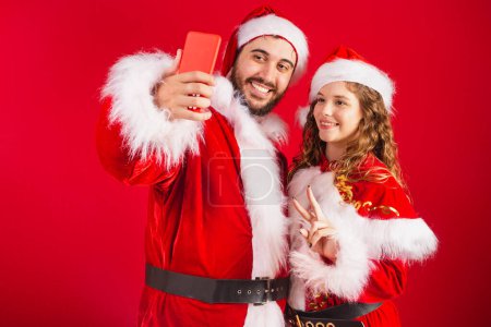 Photo for Brazilian couple, dressed in Christmas clothes, Santa Claus, using smartphone, online. - Royalty Free Image