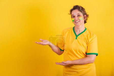 Téléchargez les photos : Adulte femme adulte, fan de football brésilien, présentant quelque chose à gauche, photo de publicité. - en image libre de droit