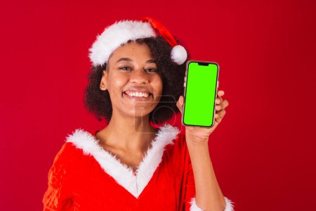 Téléchargez les photos : Belle femme brésilienne noire, habillée comme Santa Claus, maman Claus, montrant écran de smartphone - en image libre de droit