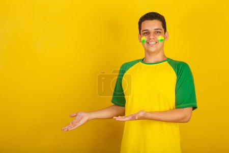 Téléchargez les photos : Jeune Brésilien fan de foot. habillé en vert, présentant quelque chose - en image libre de droit