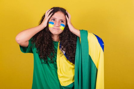 Foto de Chica brasileña, caucásica, fanática del fútbol, preocupada, ansiosa, incertidumbre. Las manos en la cabeza. - Imagen libre de derechos