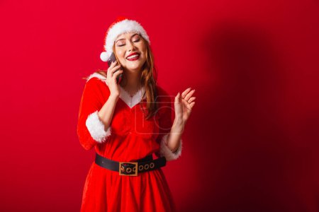 Téléchargez les photos : Belle femme rousse brésilienne, vêtue de vêtements de Noël, le Père Noël. parler sur appel vocal par smartphone. - en image libre de droit