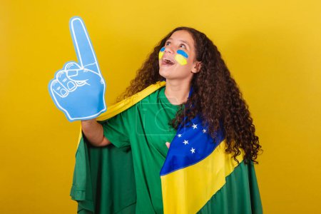 Foto de Brasileña, Caucásica, fanática del fútbol con la mano de espuma vitoreando por la copa del mundo, fanática del fútbol, ropa de fans brasileña. - Imagen libre de derechos