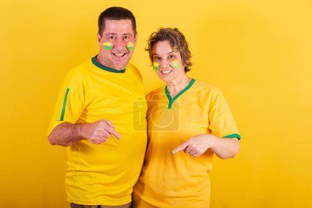 Téléchargez les photos : Couple adulte, fan de football brésilien, pointant vers le centre, seulement ici. photo publicitaire. - en image libre de droit