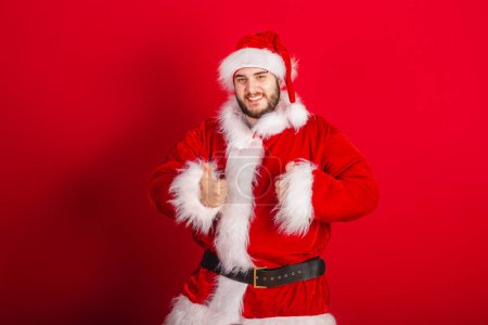 Photo for Caucasian, Brazilian man dressed in Christmas outfit, Santa Claus. Like with your fingers. - Royalty Free Image