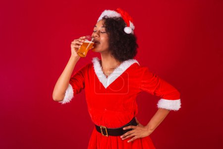 Téléchargez les photos : Belle femme brésilienne noire, habillée comme Santa Claus, maman Claus, boire de la bière - en image libre de droit