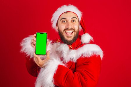 Téléchargez les photos : Homme brésilien, habillé en santa claus vêtements, tenant smartphone avec écran chromatique vert - en image libre de droit