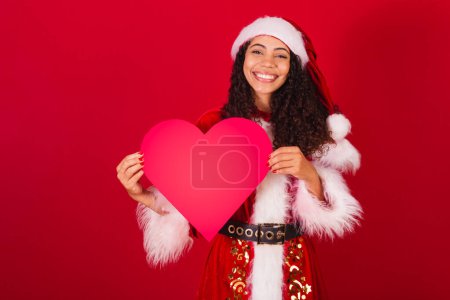 Photo for Beautiful brazilian black woman, dressed as santa claus, christmas clothes. holding red heart. - Royalty Free Image