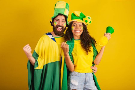 Photo for Couple of brazil soccer supporters, dressed in the colors of the nation, black woman, caucasian man. using flag and accessories - Royalty Free Image