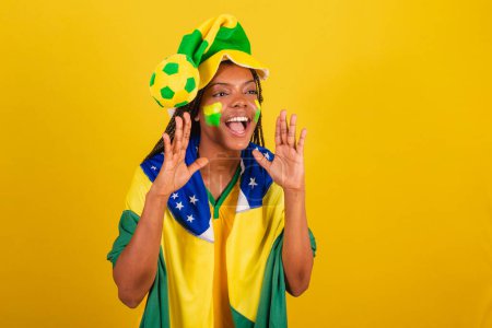 Foto de Mujer negra joven aficionada al fútbol brasileño. promoción gritando, anunciando descuento, publicidad. - Imagen libre de derechos