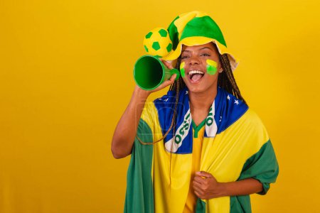 Foto de Mujer negra joven aficionada al fútbol brasileño. usando el teléfono recoger para anunciar algo. - Imagen libre de derechos