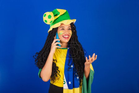 Téléchargez les photos : Jeune Brésilien noir, fan de foot. parler par appel vocal. appel vocal par smartphone. - en image libre de droit