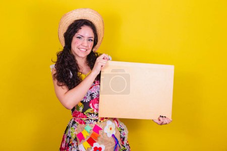 Photo for Beautiful woman dressed in typical clothes for a Festa Junina. holding sign for text or ad, advertisement. - Royalty Free Image