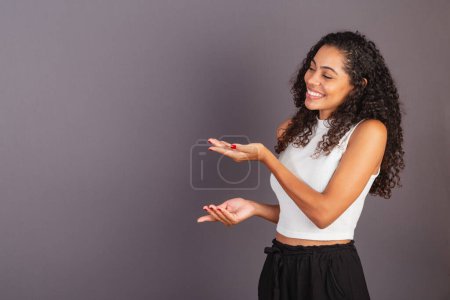 Téléchargez les photos : Jeune femme noire brésilienne présentant avec ses mains à gauche, photo de publicité. - en image libre de droit