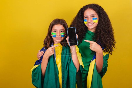 Photo for Sisters and friends cheerleaders from brazil, soccer fans, pointing to cellphone, internet, connected world, cellphone app. World Cup. Olympics. - Royalty Free Image