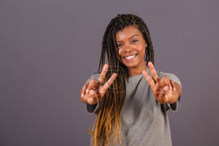 Foto de Joven mujer brasileña afro, manos hacia adelante, dedos en paz y amor. Deseándote buenas vibraciones. - Imagen libre de derechos