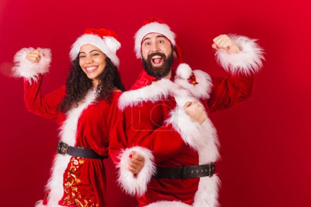 Photo for Brazilian couple, dressed for christmas, santa claus, mummy claus. Celebrating, black woman and caucasian man. - Royalty Free Image