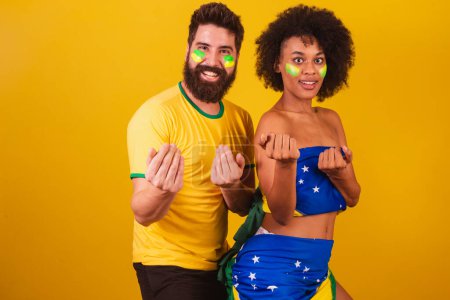 Téléchargez les photos : Couple de fans de football brésilien, habillé dans les couleurs du brésil, femme noire, homme caucasien. invitant les mains. appel, bienvenue - en image libre de droit
