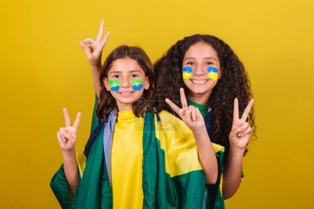 Téléchargez les photos : Sœurs et amis supporters du Brésil, fans de football, posant pour une photo, doigts de paix et d'amour, photo amusante, souriant. Coupe du Monde. Jeux olympiques. - en image libre de droit