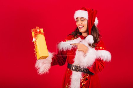 Photo for Brazilian woman dressed in Christmas clothes, Santa Claus. showing a yellow gift. - Royalty Free Image