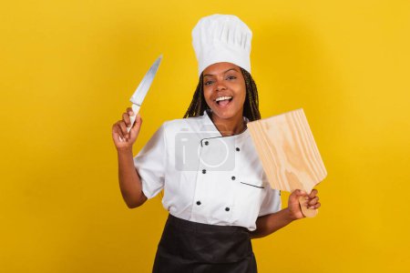 Photo for Young afro brazilian woman, chef cook, holding wooden board and knife. - Royalty Free Image