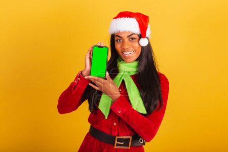 Foto de Hermosa mujer brasileña negra, vestida con ropa de navidad, santa claus, teléfono inteligente y pantalla de croma verde. - Imagen libre de derechos