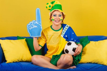 Photo for Caucasian, redhead, Brazilian, Brazilian soccer fan on couch with foam finger and ball partying - Royalty Free Image