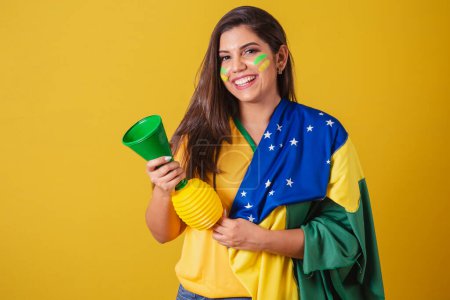 Photo for Woman supporter of Brazil, world cup 2022, soccer championship, using brazil flag as cover. honking and partying at football match. Horn. - Royalty Free Image