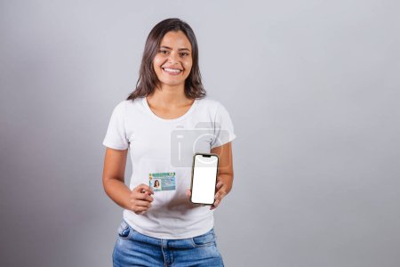 Photo for Brazilian woman, with driver's license, CNH, document. Smartphone, white screen for advertisements. - Royalty Free Image